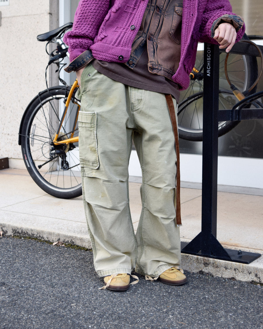 フラップポケットや膝のタック、裾のドローコードなど、ミリタリーのディテールをふんだんに取り入れた一本。内側に配置されることの多いポケットをあえて外側に設けたカーゴポケットが特徴です。ムラ糸で織り上げたバックサテン生地は、ハリとコシのある質感が魅力。さらに、水や薬品の使用を抑えながら生地の凹凸を際立たせる特殊エイジング加工を施し、深みのあるオリーブカラーに仕上げています。