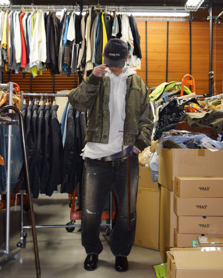 ANACHRONORM定番のレギュラーテーパード5Pパンツをベースに、リメイクで再構築した一本。
腰回りにはゆとりを持たせつつ、裾へ向かってすっきりと収まる美しいテーパードシルエットが特徴です。
タテ糸は硫化ロープ染色を施した芯白仕様で、ブラックからグレーへ自然にフェードする豊かな経年変化が魅力。
ムラ糸が生み出す自然な陰影により、ヴィンテージライクな表情を楽しめます。
さらにタテヨコに硫化ブラックのスラブ糸を使用し、ベーストーンを抑えながらもアタリを際立たせた奥行きのあるコントラストを表現。
リアルなユーズド感を備えた、加工映えする一本に仕上げています。
A reconstructed take on ANACHRONORM’s classic Regular Tapered 5P Pants, refined through its remake design.
The fit offers room around the waist with a clean taper toward the hem, ensuring both comfort and sharp lines.
Warp yarns a