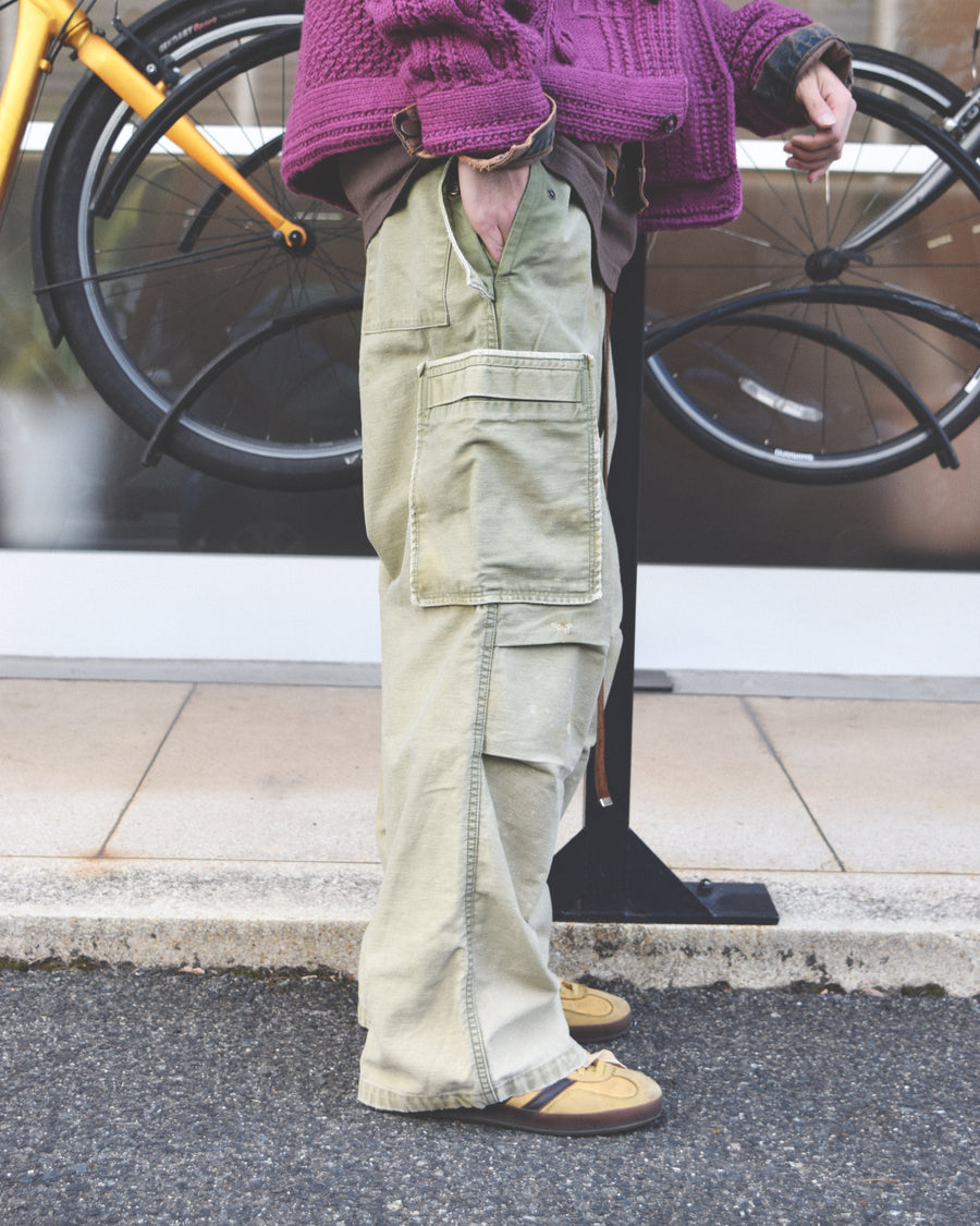 フラップポケットや膝のタック、裾のドローコードなど、ミリタリーのディテールをふんだんに取り入れた一本。内側に配置されることの多いポケットをあえて外側に設けたカーゴポケットが特徴です。ムラ糸で織り上げたバックサテン生地は、ハリとコシのある質感が魅力。さらに、水や薬品の使用を抑えながら生地の凹凸を際立たせる特殊エイジング加工を施し、深みのあるオリーブカラーに仕上げています。