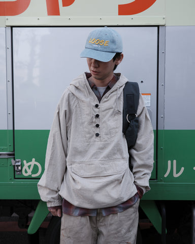 フード口のボタンの開閉により、首周りのニュアンスを自在に調整できる一着。素材には、麻カスや節を活かしたネップ糸を織り交ぜたコットンリネンチェックを採用しました。ドライタッチな生地にワンウォッシュを施すことで、麻特有のハリ感を残しつつ、肌馴染みの良い柔らかな風合いと豊かな表情を引き出しています。

This piece features adjustable hood buttons to alternate between a clean look and a relaxed neckline. Crafted from a cotton-linen check weave with rustic nep yarns, it highlights the natural texture of the fibers. The BEIGE fabric is one-washed to balance a crisp, dry touch with a soft, broken-in feel, creating a sophisticated yet comfortable aesthetic.