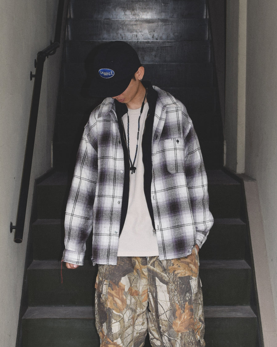 ANACHRONORMで以前リリースしていたリサイズシャツのシルエットをリファインした、ワイドシルエットシャツです。
随所に施された細かなステッチワークやダメージ加工にもご注目ください。
生地はリサイクルコットンとポリエステルを混紡したT/Cネップチェックで、起毛によるネップの風合いとメランジ染めの独特なムラ感が特徴です。
サスティナブルブリーチ加工とダメージ加工を施しており、環境に配慮しつつPURPLE×BLACKカラーで仕上げています。