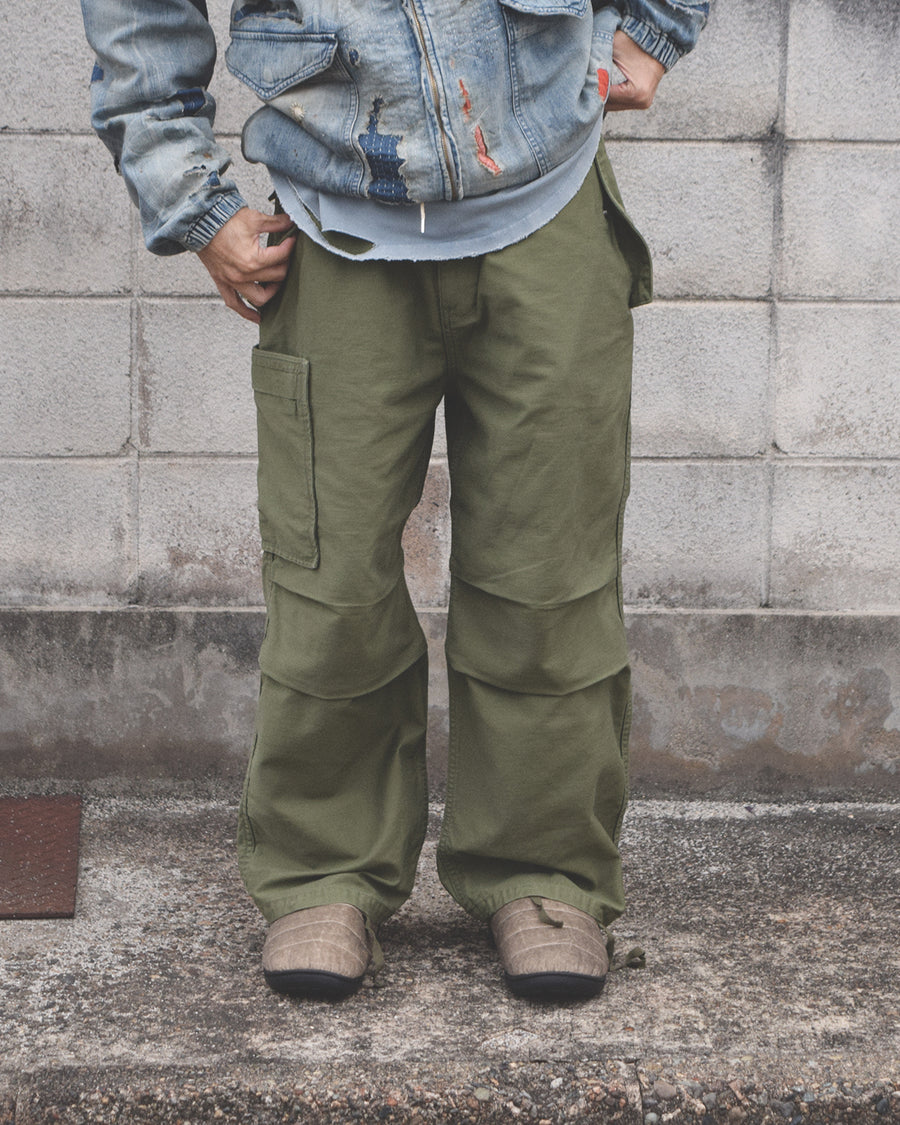 フラップポケットや膝のタック、裾のドローコードなど、ミリタリーディテールを随所に取り入れた1本。通常は内側に配置されるポケットをあえて外側に設けたカーゴポケットが印象的です。ムラ糸で織り上げたバックサテン生地は、独特のハリとコシを持ち、深みのあるオリーブカラーが魅力です。
