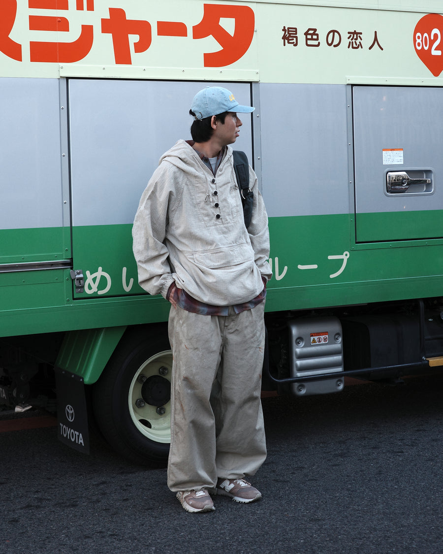 フード口のボタンの開閉により、首周りのニュアンスを自在に調整できる一着。素材には、麻カスや節を活かしたネップ糸を織り交ぜたコットンリネンチェックを採用しました。ドライタッチな生地にワンウォッシュを施すことで、麻特有のハリ感を残しつつ、肌馴染みの良い柔らかな風合いと豊かな表情を引き出しています。

This piece features adjustable hood buttons to alternate between a clean look and a relaxed neckline. Crafted from a cotton-linen check weave with rustic nep yarns, it highlights the natural texture of the fibers. The BEIGE fabric is one-washed to balance a crisp, dry touch with a soft, broken-in feel, creating a sophisticated yet comfortable aesthetic.