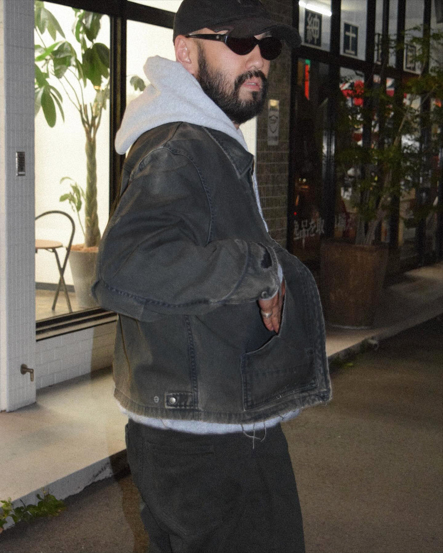 【 商品名：リメイクデトロイトダックジャケット 】

本製品は、ゆとりのある身幅とややクロップド丈に設計されたブラックカラーのジャケットで、インナーアイテムとのレイヤードを楽しめるバランスの良いシルエットが特徴です。生地には頒布の中でも最も薄手の11号帆布生地を採用しており、強度・耐久性に優れ、着用を重ねるごとにアタリなどの経年変化を味わえる素材です。さらに、水や薬品の使用量を抑えながら生地の凹凸部分のアタリを強調し、同時に自然な脱色感を生み出す特殊エイジング加工を施し、加えてサンフェードによるダメージ加工を加えることで、より奥行きのある表情に仕上げています。