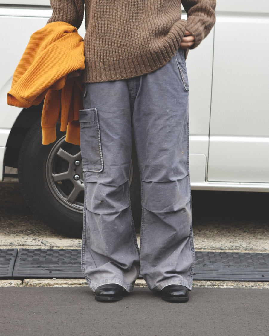 フラップポケットや膝のタック、裾のドローコードなど、ミリタリーのディテールをふんだんに取り入れた一本。内側に配置されることの多いポケットをあえて外側に設けたカーゴポケットが特徴です。ムラ糸で織り上げたバックサテン生地は、ハリとコシのある質感が魅力。さらに、水や薬品の使用を抑えながら生地の凹凸を際立たせる特殊エイジング加工を施し、深みのあるネイビーカラーに仕上げています。