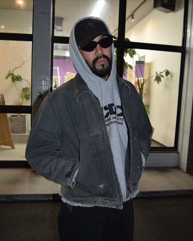 【 商品名：リメイクデトロイトダックジャケット 】

本製品は、ゆとりのある身幅とややクロップド丈に設計されたブラックカラーのジャケットで、インナーアイテムとのレイヤードを楽しめるバランスの良いシルエットが特徴です。生地には頒布の中でも最も薄手の11号帆布生地を採用しており、強度・耐久性に優れ、着用を重ねるごとにアタリなどの経年変化を味わえる素材です。さらに、水や薬品の使用量を抑えながら生地の凹凸部分のアタリを強調し、同時に自然な脱色感を生み出す特殊エイジング加工を施し、加えてサンフェードによるダメージ加工を加えることで、より奥行きのある表情に仕上げています。