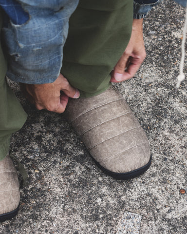 リラックスサンダル〈SUBU〉とのコラボレーションによって生まれた、特別仕様のフットギア。
アッパーにはANACHRONORMが独自の加工を施したナイロンオックスを採用。
染料の濃度や色味を幾度も検証し、洗いをかけることで偶発的なムラや陰影が生まれ、ひとつひとつランダムな表情を持つ一足が完成しました。
ふんわりと包み込む起毛ライニングと4層構造のインソールが、ダウンのようなぬくもりと心地よい弾力を生み出します。
SUBUの機能性にANACHRONORMのクラフト感が融合した、冬の定番を新たに更新する一足です。
カラーはベージュ。