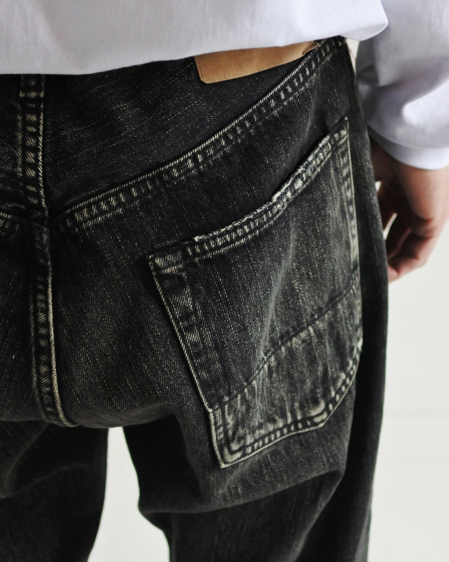 ANACHRONORM定番のレギュラーテーパード5Pパンツをベースに、リメイクで再構築した一本。
腰回りにはゆとりを持たせつつ、裾へ向かってすっきりと収まる美しいテーパードシルエットが特徴です。
タテ糸は硫化ロープ染色を施した芯白仕様で、ブラックからグレーへ自然にフェードする豊かな経年変化が魅力。
ムラ糸が生み出す自然な陰影により、ヴィンテージライクな表情を楽しめます。
さらにタテヨコに硫化ブラックのスラブ糸を使用し、ベーストーンを抑えながらもアタリを際立たせた奥行きのあるコントラストを表現。
リアルなユーズド感を備えた、加工映えする一本に仕上げています。
A reconstructed take on ANACHRONORM’s classic Regular Tapered 5P Pants, refined through its remake design.
The fit offers room around the waist with a clean taper toward the hem, ensuring both comfort and sharp lines.
Warp yarns a