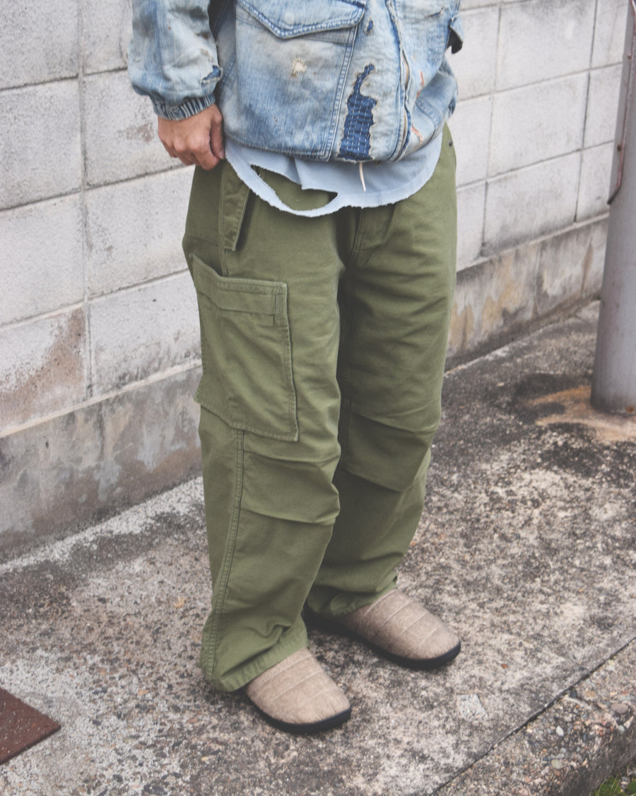 フラップポケットや膝のタック、裾のドローコードなど、ミリタリーディテールを随所に取り入れた1本。通常は内側に配置されるポケットをあえて外側に設けたカーゴポケットが印象的です。ムラ糸で織り上げたバックサテン生地は、独特のハリとコシを持ち、深みのあるオリーブカラーが魅力です。