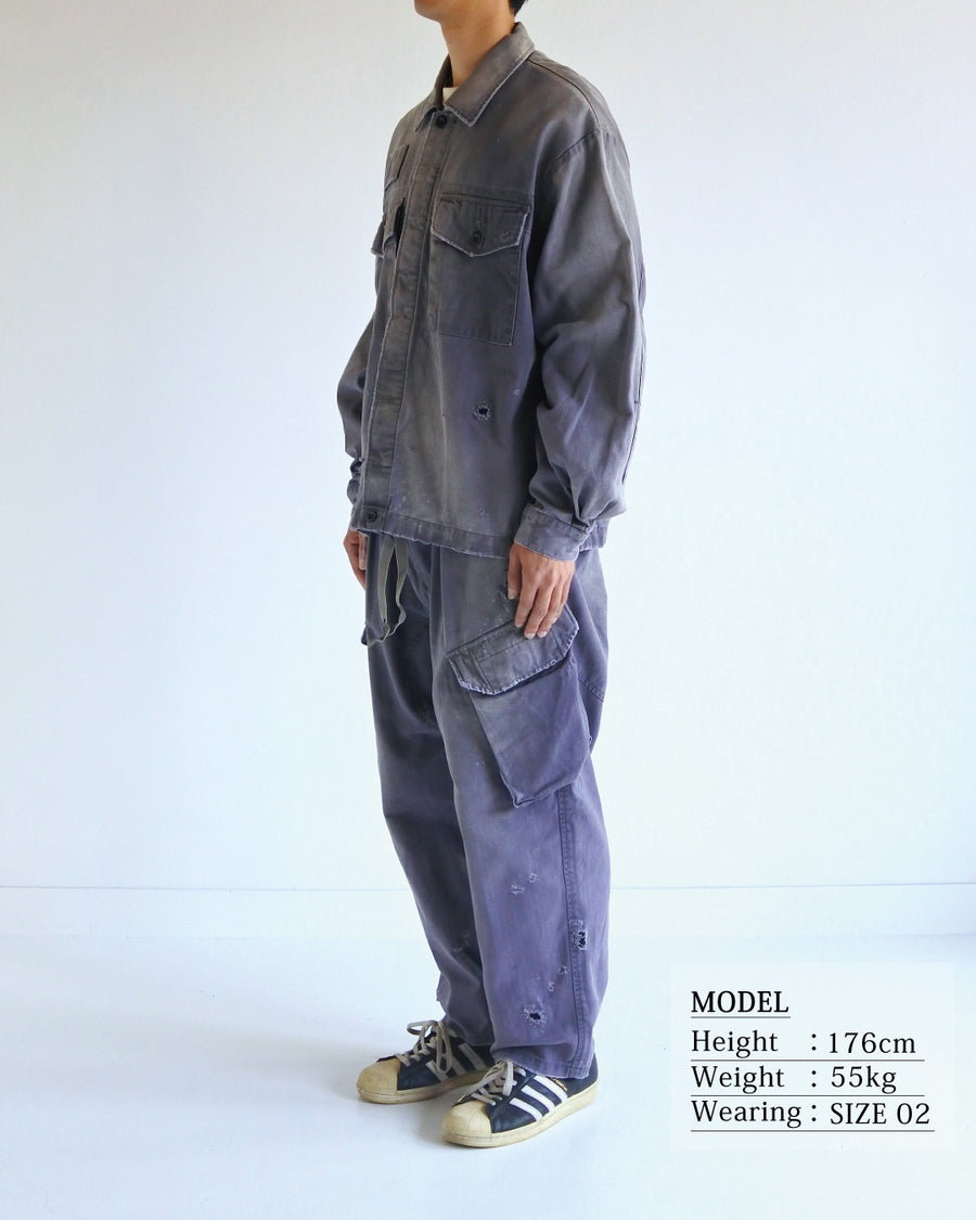 ミリタリーのシャツジャケットを現代的シルエットに更新。裾のドローコードでスタイルに合わせた変化を楽しめます。素材には肌馴染みの良い10sヘリンボンを採用。環境に配慮した特殊エイジング・サンフェード加工とダメージ加工を施すことで、クラシカルな生地にリアリティのある褪色感とヴィンテージライクな佇まいを表現しました。

A modern military shirt jacket with hem drawcords for an adjustable silhouette. Crafted from soft 10s herringbone, this CHARCOAL piece undergoes a special sun-fade and damage process. It achieves a realistic, time-worn vintage look with authentic distressing while minimizing environmental impact through eco-conscious processing.