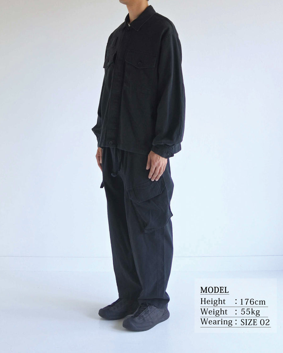 ミリタリーのシャツジャケットを現代的シルエットに更新。裾のドローコードで着丈のニュアンスを自在に調整可能です。素材には、やや甘織りで肌馴染みの良い10sヘリンボンを採用。ストーンバイオウォッシュを施すことで、クラシカルな生地感に柔らかな風合いとこなれ感をプラスした、着回し力の高い一着に仕上げました。

A modern update to the classic military shirt jacket, featuring hem drawcords for an adjustable silhouette. Crafted from 10s herringbone, slightly loose-knitted for a soft, comfortable touch. This BLACK piece has been treated with a stone bio-wash, giving the traditional weave a natural, worn-in texture and a sophisticated casual feel.