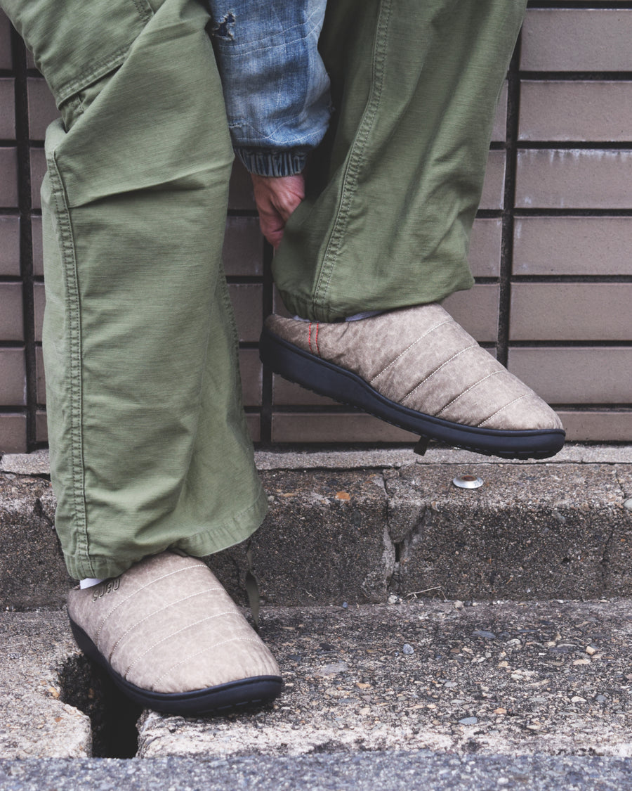 リラックスサンダル〈SUBU〉とのコラボレーションによって生まれた、特別仕様のフットギア。
アッパーにはANACHRONORMが独自の加工を施したナイロンオックスを採用。
染料の濃度や色味を幾度も検証し、洗いをかけることで偶発的なムラや陰影が生まれ、ひとつひとつランダムな表情を持つ一足が完成しました。
ふんわりと包み込む起毛ライニングと4層構造のインソールが、ダウンのようなぬくもりと心地よい弾力を生み出します。
SUBUの機能性にANACHRONORMのクラフト感が融合した、冬の定番を新たに更新する一足です。
カラーはベージュ。