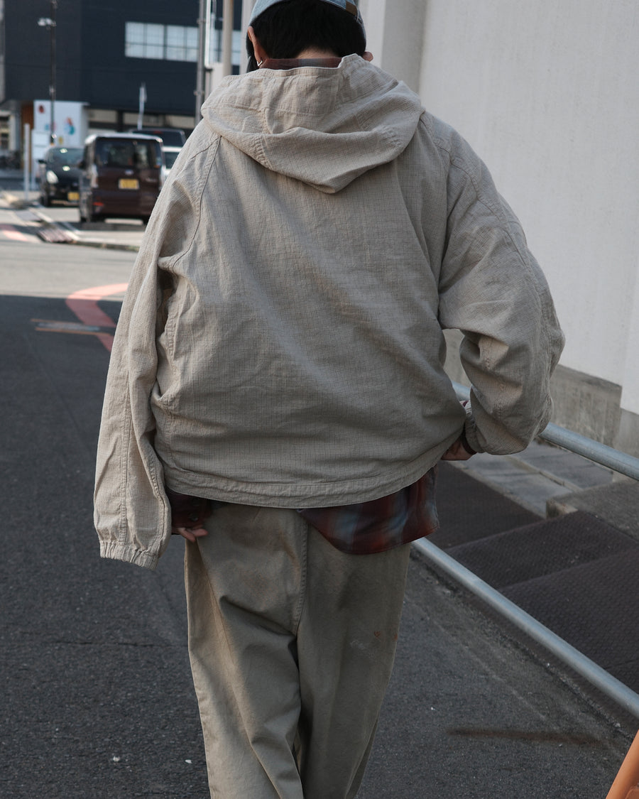 フード口のボタンの開閉により、首周りのニュアンスを自在に調整できる一着。素材には、麻カスや節を活かしたネップ糸を織り交ぜたコットンリネンチェックを採用しました。ドライタッチな生地にワンウォッシュを施すことで、麻特有のハリ感を残しつつ、肌馴染みの良い柔らかな風合いと豊かな表情を引き出しています。

This piece features adjustable hood buttons to alternate between a clean look and a relaxed neckline. Crafted from a cotton-linen check weave with rustic nep yarns, it highlights the natural texture of the fibers. The BEIGE fabric is one-washed to balance a crisp, dry touch with a soft, broken-in feel, creating a sophisticated yet comfortable aesthetic.