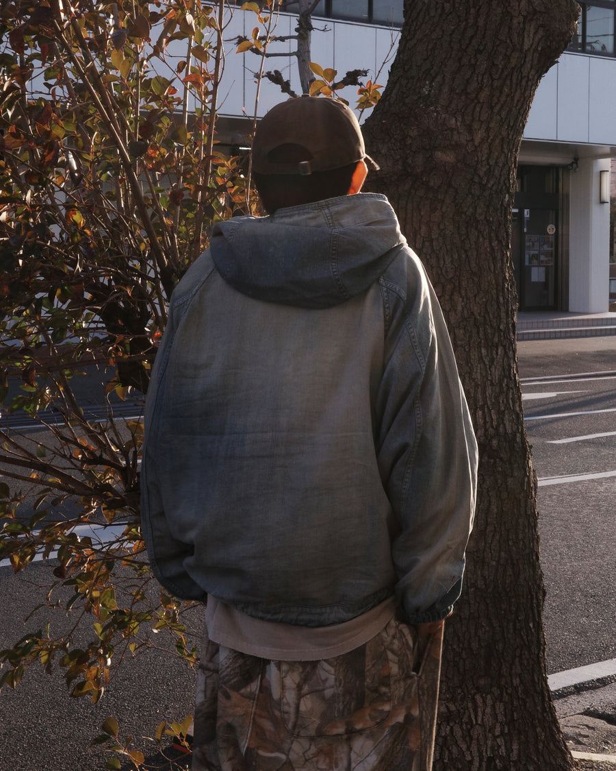 フード口のボタンの開閉により、首まわりのニュアンスを変えて楽しめる一着。素材には、経糸にコットンムラ糸、緯糸に綿麻混紡糸を使用した綿麻6ozデニムを採用しました。シャープなムラ感とリネン混ならではの粗野な風合いが、ヴィンテージの魅力を引き立てます。エイジング加工を施すことで、全体にリアリティのあるアタリ感を出し、長年着込んだような深みのある表情に仕上げました。A versatile piece featuring adjustable hood buttons to create a clean or relaxed neckline. Crafted from 6oz cotton-linen denim, the fabric combines sharp slub textures with a rustic linen feel for an authentic vintage character. Treated with an aging process to create realistic wear and fade, this INDIGO garment offers a sophisti