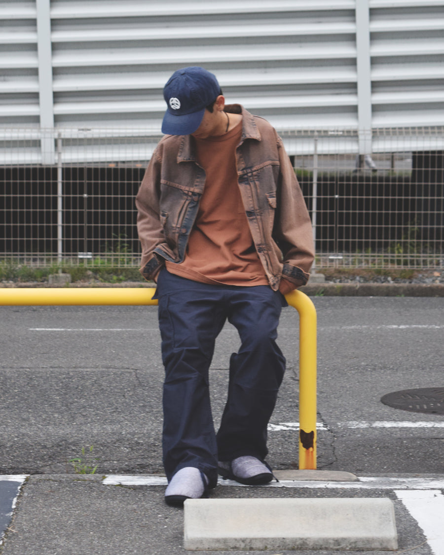 フラップポケットや膝のタック、裾のドローコードなど、ミリタリーディテールを随所に取り入れた1本。通常は内側に配置されるポケットをあえて外側に設けたカーゴポケットが印象的です。ムラ糸で織り上げたバックサテン生地は、独特のハリとコシを持ち、深みのあるネイビーカラーが魅力です。