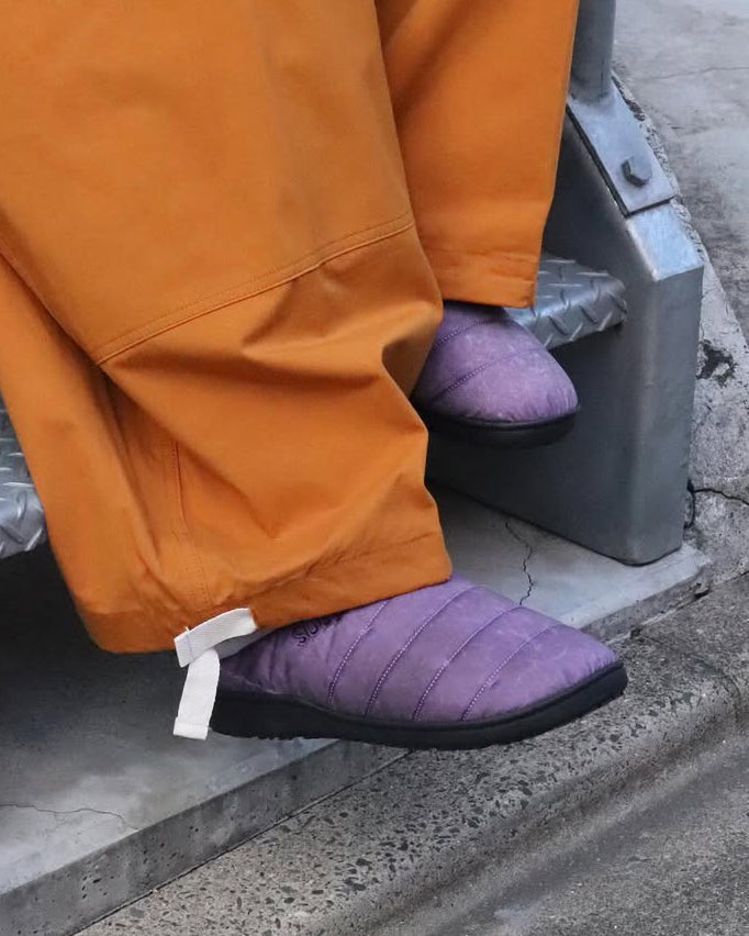 リラックスサンダル〈SUBU〉とのコラボレーションによって生まれた、特別仕様のフットギア。
アッパーにはANACHRONORMが独自の加工を施したナイロンオックスを採用。
染料の濃度や色味を幾度も検証し、洗いをかけることで偶発的なムラや陰影が生まれ、ひとつひとつランダムな表情を持つ一足が完成しました。
ふんわりと包み込む起毛ライニングと4層構造のインソールが、ダウンのようなぬくもりと心地よい弾力を生み出します。
SUBUの機能性にANACHRONORMのクラフト感が融合した、冬の定番を新たに更新する一足です。
カラーはパープル。