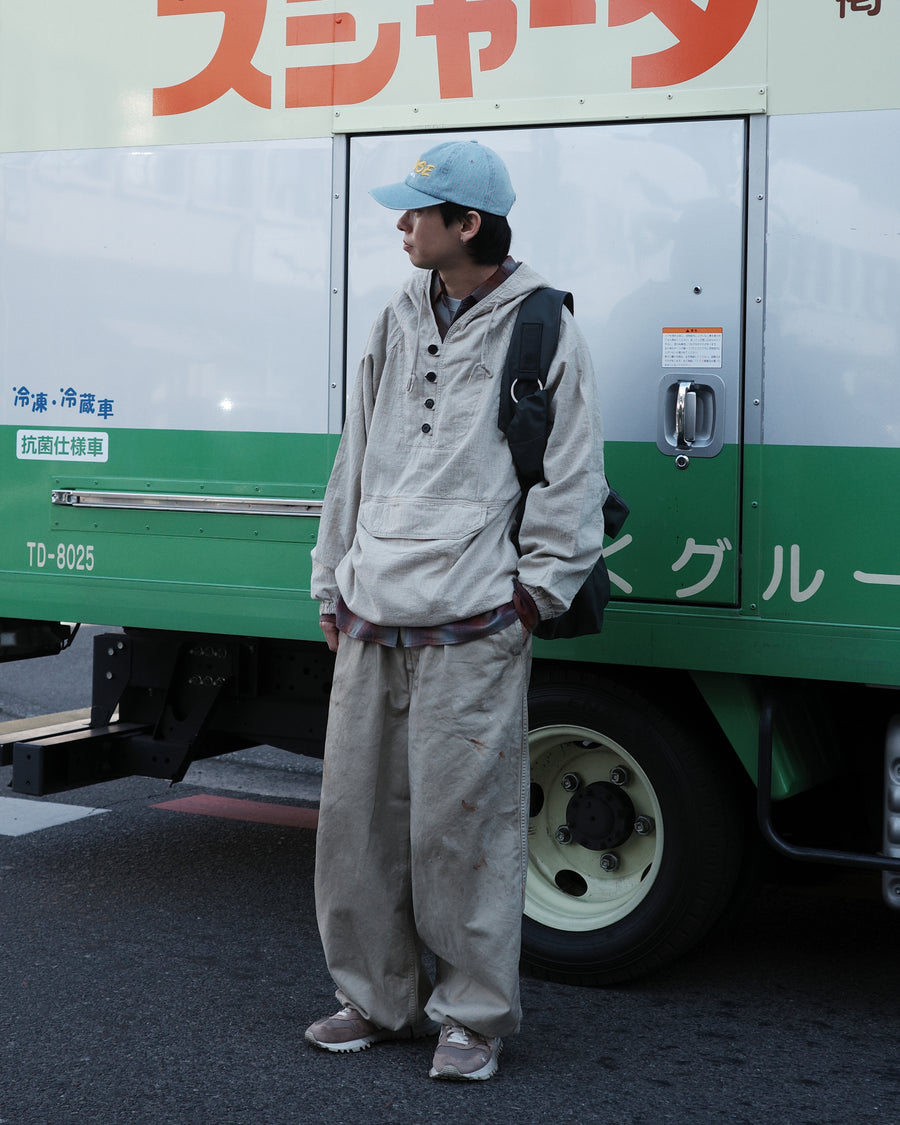 フロントに2タックを施し、ワタリから裾にかけてゆとりを持たせたワイルドなワイドシルエット。裾のドローコードでシルエットの変化も自在に楽しめます。素材には耐久性に優れ、綾織特有の柔らかさを持つ厚手チノクロスを採用。ストーンバイオウォッシュと汚し加工を重ねることで、長年穿き込んだようなリアルな質感と深みのある表情を引き出しました。

Wild, wide-silhouette pants with double-tucked fronts and adjustable hem drawcords. Crafted from durable, soft chino cloth, this BEIGE pair features a stone bio-wash and staining process. This creates an authentic, rugged texture and a deeply weathered look, blending vintage workwear aesthetics with a modern, voluminous fit.