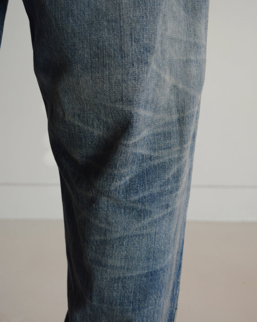 1985年のLEVIS 550をベースに再構築した、ワイドテーパードのリメイク5Pデニム。
12.5ozデニムのタテ糸には中白のインディゴロープ染色糸を使用し、ムラ感のある豊かな表情を演出。タテ落ちとインディゴの濃淡を活かすことで、ヴィンテージにはない独自の風合いを表現しています。さらに手作業のトーンコントロールと特別なエイジング加工を加えることで奥行きある仕上がりに。オリジナル染料の吹き付けにより、モダンでソリッドな印象も併せ持つ一本です。This remade 5P denim features a wide tapered silhouette inspired by the 1985 LEVIS 550.
The 12.5oz denim uses medium-white indigo rope–dyed warp yarns, giving it a textured, slubby character.
By highlighting vertical fading and vivid indigo variations, it achieves a look distinct from vin