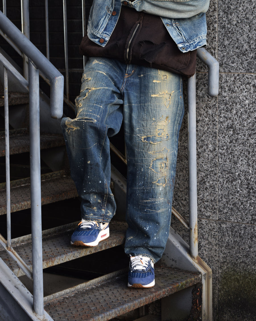 12.5ozデニムを使用したテーパードシルエット。
濃色エイジングとブリーチを組み合わせたハードダメージ加工。
複数の当て布でパッチワークリメイクを施した存在感ある一本です。
A tapered silhouette crafted from 12.5oz denim.
Features heavy damage with dark aging and bleach treatments.
Finished with patchwork-style remake details using multiple fabric patches.