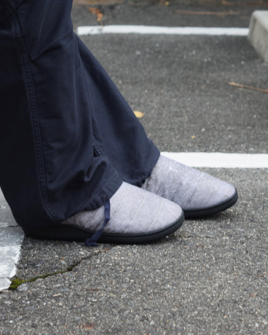 リラックスサンダル〈SUBU〉とのコラボレーションによって生まれた、特別仕様のフットギア。
アッパーにはANACHRONORMが独自の加工を施したナイロンオックスを採用。
染料の濃度や色味を幾度も検証し、洗いをかけることで偶発的なムラや陰影が生まれ、ひとつひとつランダムな表情を持つ一足が完成しました。
ふんわりと包み込む起毛ライニングと4層構造のインソールが、ダウンのようなぬくもりと心地よい弾力を生み出します。
SUBUの機能性にANACHRONORMのクラフト感が融合した、冬の定番を新たに更新する一足です。
カラーはホワイト。