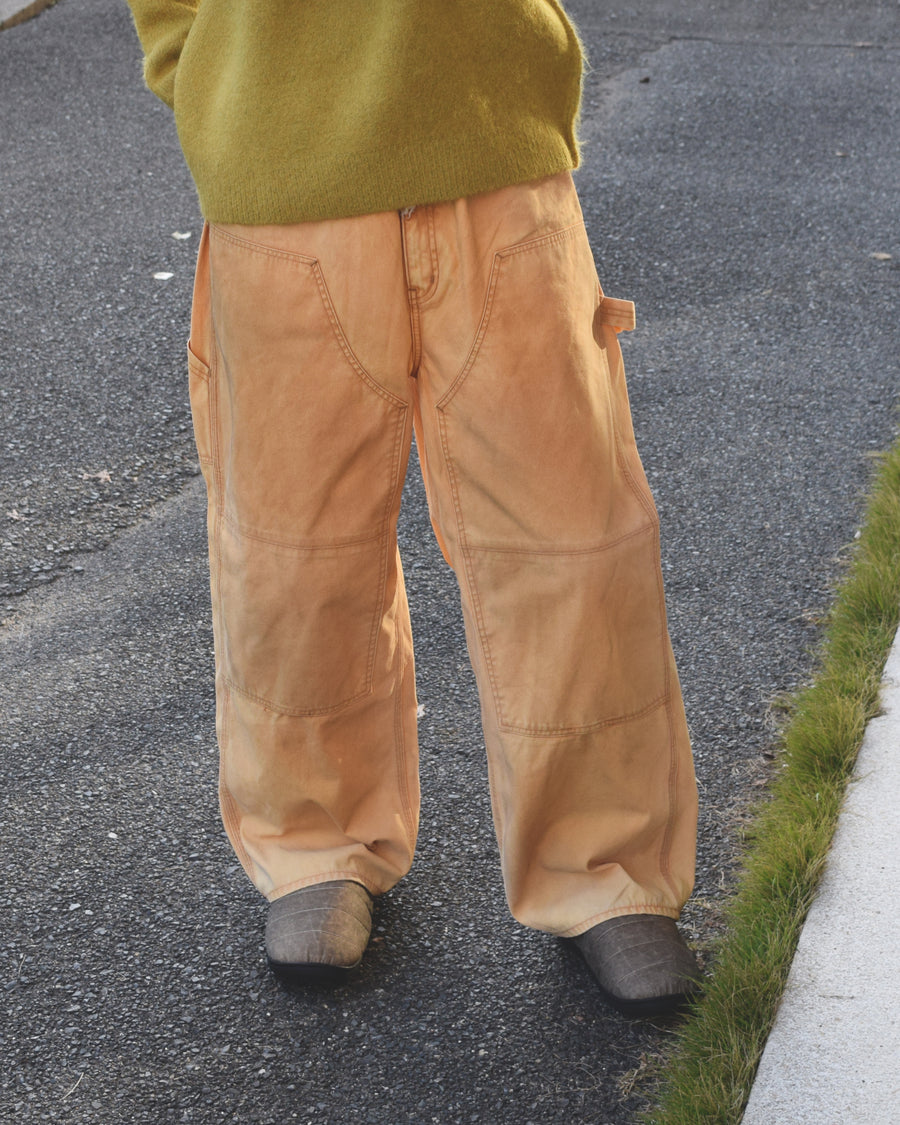 【 商品名：ダブルニーダックペインターパンツ 】

本製品は、レングスをやや長めに設定したイエローカラーのペインターパンツです。ウエスト部分にはナイロンオックス生地で切り替えを施し、ワーク感を抑えたデザインに仕上げています。生地には頒布の中でも最も薄手の11号帆布生地を使用しており、強度・耐久性に優れるだけでなく、着用を重ねるごとにアタリなどの経年変化を楽しめる素材です。また、水や薬品の使用量を抑えつつ生地の凹凸部分のアタリを強調し、同時に自然な脱色感を生み出す特殊エイジング加工を施しています。