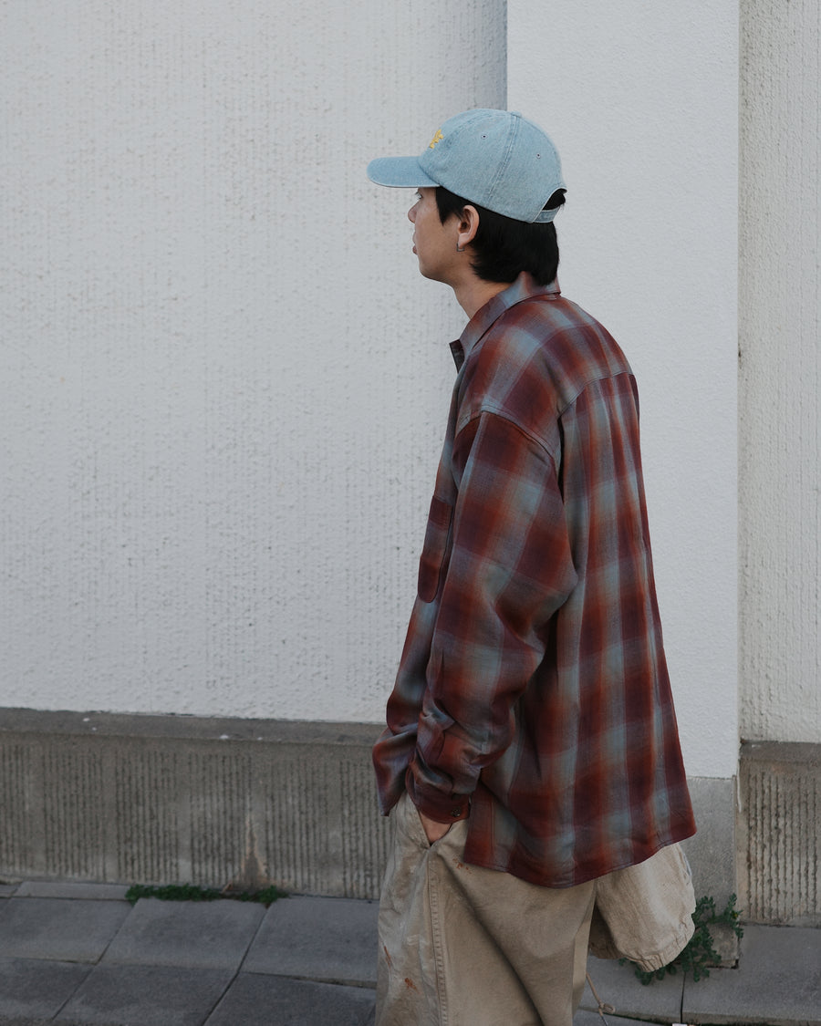 オンブレチェック柄が目を惹くオープンカラーシャツ。生地が持つ自然なドレープ感を活かし、リラックス感のあるゆとりを持たせたシルエットに仕上げました。素材にはタテ・ヨコ共にレーヨン糸を使用したレーヨンチェックを採用。非常に優れた落ち感と、袖を通した瞬間に感じる滑らかで心地よい肌触りが、上質なリラックススタイルを演出します。

An open-collar shirt featuring a classic ombre check pattern. The relaxed silhouette highlights the natural drape and fluid movement of the fabric. Crafted from a high-quality rayon check weave, this RED CHECK piece is characterized by its exceptional softness and smooth touch, offering a sophisticated look with an effortlessly comfortable feel.