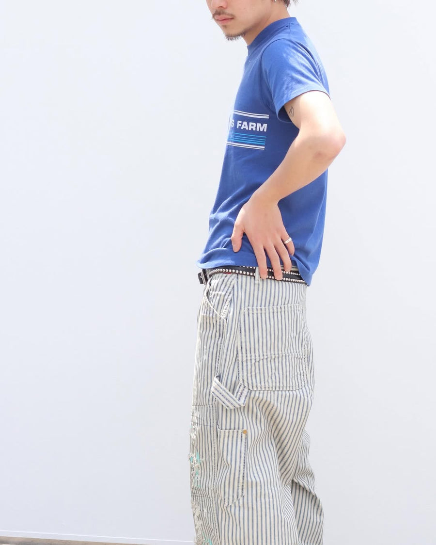 過去の定番ダブルニーペインターパンツをリファインし、腰回りにゆとりを持たせたワイドストレートシルエットに仕上げたヒッコリーパンツ。
岡山県井原市製の9ozヒッコリーストライプ生地を使用し、ハリのある風合いが特徴。
全体にエイジングとハードダメージを施し、手作業のステッチ補修やランダムなペンキでリアルな表情を加えています。