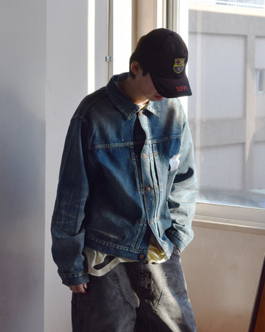 70502XX（1stタイプ）をベースに、現代的なシルエットとディテールへリファインしたベーシックな一着。旧式力織機で織り上げた12.5ozセルビッチデニムを使用し、中白糸による自然なムラ感を活かしています。ハードなアタリとリペア跡を再現したエイジングリメイクに加え、最終工程の汚し加工でヴィンテージ特有の枯れた表情を追求。伝統的な意匠に圧倒的なリアリティを宿した仕上がりです。
A refined 1st-type denim jacket in 12.5oz selvedge denim. It features heavy distressing and authentic repairs to pursue an authentic, weathered vintage aesthetic. Finished with a subtle "dirty" wash for added depth, this piece seamlessly blends heritage design with a modern silhouette and a seasoned, time-worn character.
