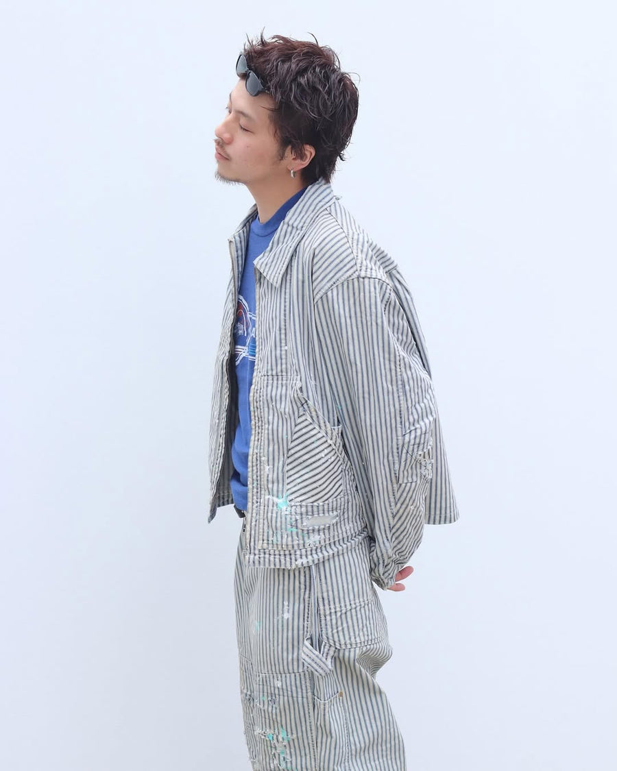 ゆとりある身幅とややクロップド丈でレイヤードを楽しめるデザインにしたヒッコリージャケット。
岡山県製9ozヒッコリーストライプ生地を使用し、ハリのあるしっかりとした風合いが特徴。
全体にエイジングとハードダメージを施し、手作業のステッチ補修とランダムなペンキでリアルな表情に仕上げています。