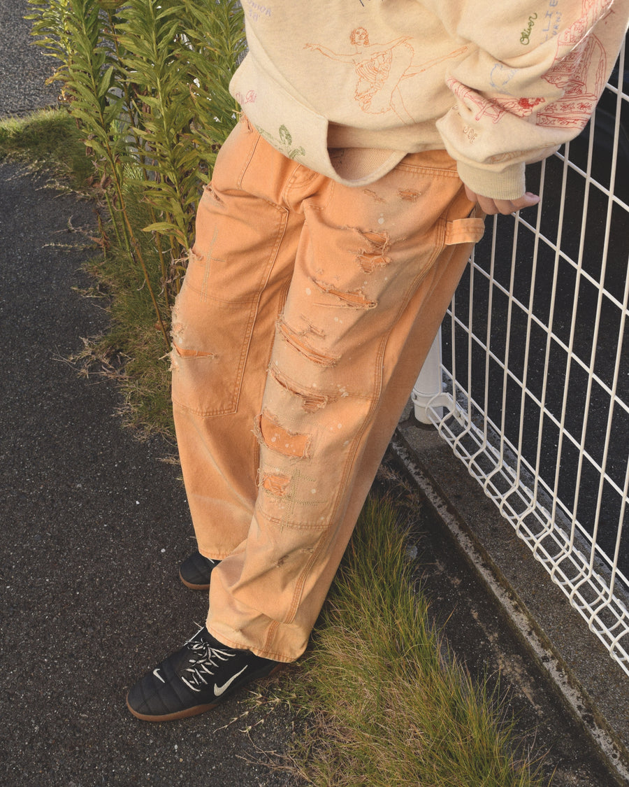 【 商品名：リメイクダブルニーダックペインターパンツ 】

本製品は、レングスをやや長めに設定したイエローカラーのペインターパンツです。ウエスト部分にはナイロンオックス生地で切り替えを施し、ワーク感を抑えたバランスの良いデザインに仕上げています。生地には頒布の中でも最も薄手の11号帆布生地を使用しており、強度・耐久性に優れるだけでなく、着用を重ねるごとにアタリなどの経年変化を味わえる素材です。また、水や薬品の使用量を抑えながら生地の凹凸部分のアタリを強調し、同時に自然な脱色感を与える特殊エイジング加工に加え、サンフェードによるダメージ加工も施すことで、より深みのある表情に仕上げています。