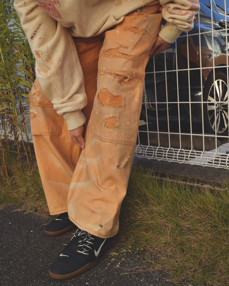 【 商品名：リメイクダブルニーダックペインターパンツ 】

本製品は、レングスをやや長めに設定したイエローカラーのペインターパンツです。ウエスト部分にはナイロンオックス生地で切り替えを施し、ワーク感を抑えたバランスの良いデザインに仕上げています。生地には頒布の中でも最も薄手の11号帆布生地を使用しており、強度・耐久性に優れるだけでなく、着用を重ねるごとにアタリなどの経年変化を味わえる素材です。また、水や薬品の使用量を抑えながら生地の凹凸部分のアタリを強調し、同時に自然な脱色感を与える特殊エイジング加工に加え、サンフェードによるダメージ加工も施すことで、より深みのある表情に仕上げています。