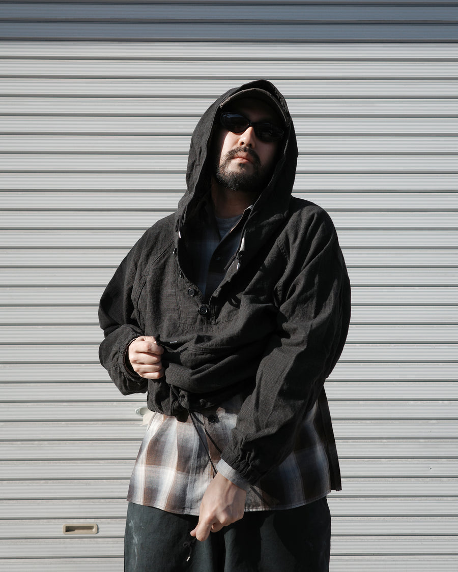 フード口のボタンの開閉により、首周りのニュアンスを自在に調整できる一着。素材には、麻カスや節を活かしたネップ糸を織り交ぜたコットンリネンチェックを採用しました。ドライタッチな生地にワンウォッシュを施すことで、麻特有のハリ感を残しつつ、肌馴染みの良い柔らかな風合いと豊かな表情を引き出しています。

This piece features adjustable hood buttons to alternate between a clean look and a relaxed neckline. Crafted from a cotton-linen check weave with rustic nep yarns, it highlights the natural texture of the fibers. The BLACK fabric is one-washed to balance a crisp, dry touch with a soft, broken-in feel, creating a sophisticated yet comfortable aesthetic.