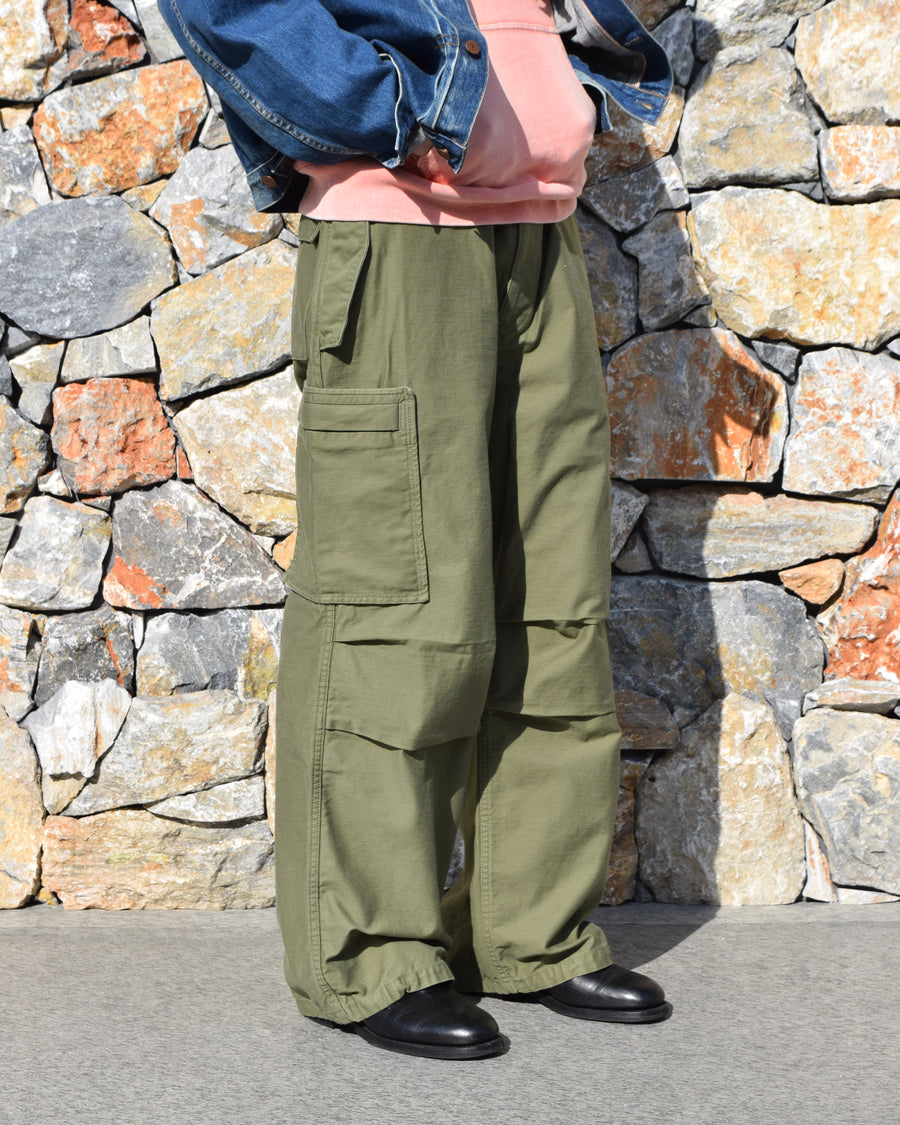 フラップポケットや膝のタック、裾のドローコードなど、ミリタリーディテールを随所に取り入れた1本。通常は内側に配置されるポケットをあえて外側に設けたカーゴポケットが印象的です。ムラ糸で織り上げたバックサテン生地は、独特のハリとコシを持ち、深みのあるオリーブカラーが魅力です。