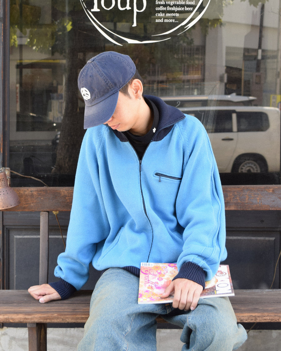 コットンニットを使用したドライバーズニット。
太番手の強撚糸による特殊な天竺編みで、適度なハリと風合いを持たせています。
ゆとりのある身幅ながら、アウターのインナーとしても使いやすいバランスの取れたシルエットに仕上げました。コットン素材のためホームクリーニングも可能です。
カラーは鮮やかなスカイブルー。