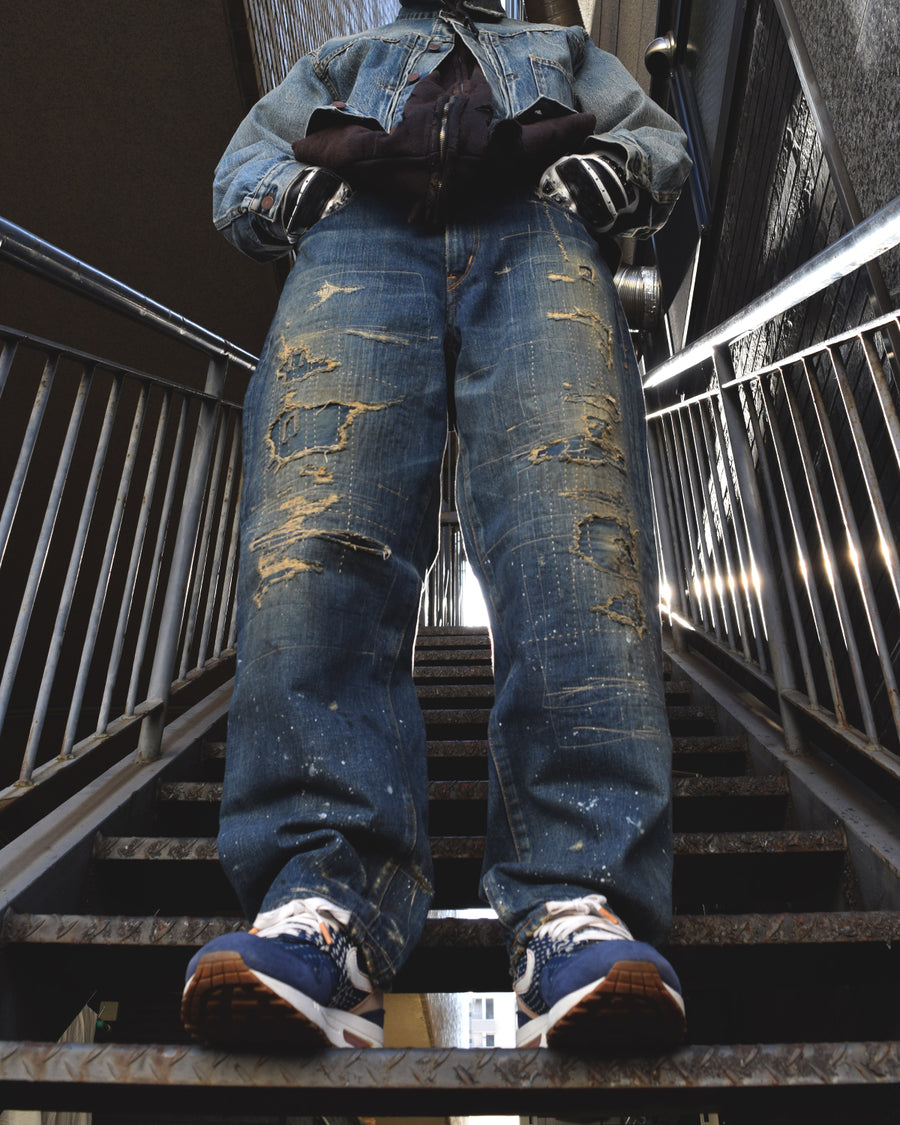 12.5ozデニムを使用したテーパードシルエット。
濃色エイジングとブリーチを組み合わせたハードダメージ加工。
複数の当て布でパッチワークリメイクを施した存在感ある一本です。
A tapered silhouette crafted from 12.5oz denim.
Features heavy damage with dark aging and bleach treatments.
Finished with patchwork-style remake details using multiple fabric patches.