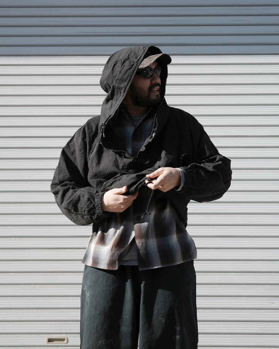 フード口のボタンの開閉により、首周りのニュアンスを自在に調整できる一着。素材には、麻カスや節を活かしたネップ糸を織り交ぜたコットンリネンチェックを採用しました。ドライタッチな生地にワンウォッシュを施すことで、麻特有のハリ感を残しつつ、肌馴染みの良い柔らかな風合いと豊かな表情を引き出しています。

This piece features adjustable hood buttons to alternate between a clean look and a relaxed neckline. Crafted from a cotton-linen check weave with rustic nep yarns, it highlights the natural texture of the fibers. The BLACK fabric is one-washed to balance a crisp, dry touch with a soft, broken-in feel, creating a sophisticated yet comfortable aesthetic.