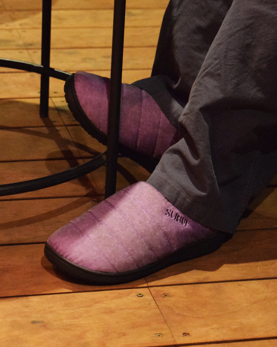リラックスサンダル〈SUBU〉とのコラボレーションによって生まれた、特別仕様のフットギア。
アッパーにはANACHRONORMが独自の加工を施したナイロンオックスを採用。
染料の濃度や色味を幾度も検証し、洗いをかけることで偶発的なムラや陰影が生まれ、ひとつひとつランダムな表情を持つ一足が完成しました。
ふんわりと包み込む起毛ライニングと4層構造のインソールが、ダウンのようなぬくもりと心地よい弾力を生み出します。
SUBUの機能性にANACHRONORMのクラフト感が融合した、冬の定番を新たに更新する一足です。
カラーはパープル。
