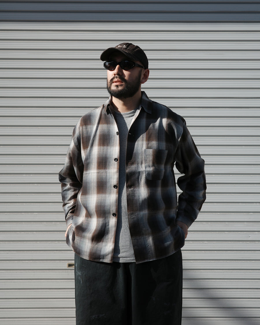 オンブレチェック柄が目を惹くオープンカラーシャツ。生地が持つ自然なドレープ感を活かし、リラックス感のあるゆとりを持たせたシルエットに仕上げました。素材にはタテ・ヨコ共にレーヨン糸を使用したレーヨンチェックを採用。非常に優れた落ち感と、袖を通した瞬間に感じる滑らかで心地よい肌触りが、上質なリラックススタイルを演出します。

An open-collar shirt featuring a classic ombre check pattern. The relaxed silhouette highlights the natural drape and fluid movement of the fabric. Crafted from a high-quality rayon check weave, this BLUE CHECK piece is characterized by its exceptional softness and smooth touch, offering a sophisticated look with an effortlessly comfortable feel.