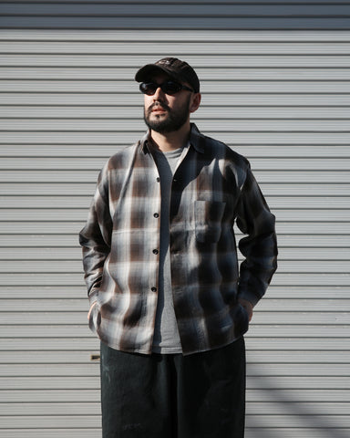 オンブレチェック柄が目を惹くオープンカラーシャツ。生地が持つ自然なドレープ感を活かし、リラックス感のあるゆとりを持たせたシルエットに仕上げました。素材にはタテ・ヨコ共にレーヨン糸を使用したレーヨンチェックを採用。非常に優れた落ち感と、袖を通した瞬間に感じる滑らかで心地よい肌触りが、上質なリラックススタイルを演出します。

An open-collar shirt featuring a classic ombre check pattern. The relaxed silhouette highlights the natural drape and fluid movement of the fabric. Crafted from a high-quality rayon check weave, this BLUE CHECK piece is characterized by its exceptional softness and smooth touch, offering a sophisticated look with an effortlessly comfortable feel.