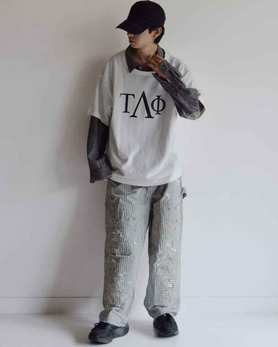 過去の定番ダブルニーペインターパンツをリファインし、腰回りにゆとりを持たせたワイドストレートシルエットに仕上げたヒッコリーパンツ。
岡山県井原市製の9ozヒッコリーストライプ生地を使用し、ハリのある風合いが特徴。
全体にエイジングとハードダメージを施し、手作業のステッチ補修やランダムなペンキでリアルな表情を加えています。