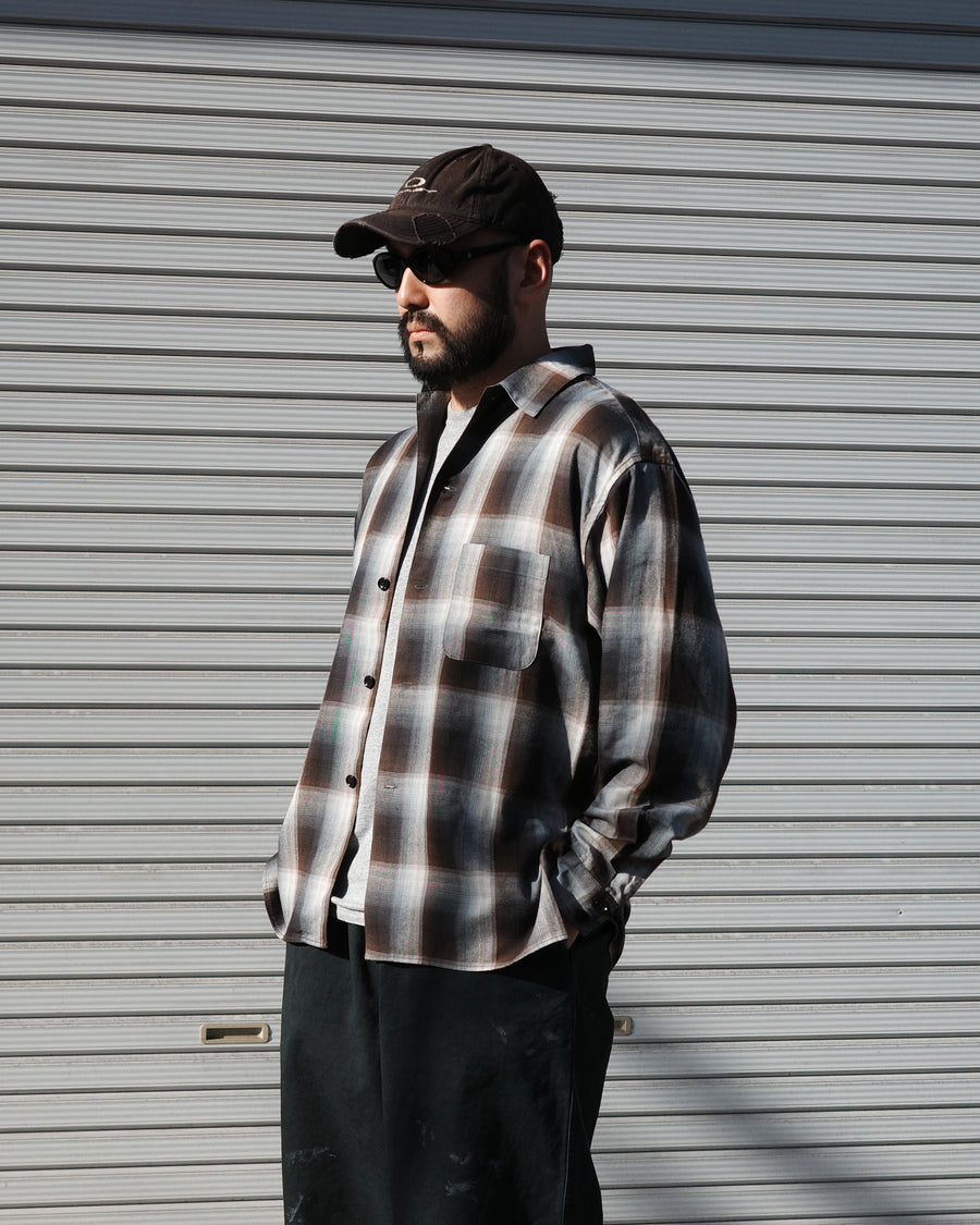 オンブレチェック柄が目を惹くオープンカラーシャツ。生地が持つ自然なドレープ感を活かし、リラックス感のあるゆとりを持たせたシルエットに仕上げました。素材にはタテ・ヨコ共にレーヨン糸を使用したレーヨンチェックを採用。非常に優れた落ち感と、袖を通した瞬間に感じる滑らかで心地よい肌触りが、上質なリラックススタイルを演出します。

An open-collar shirt featuring a classic ombre check pattern. The relaxed silhouette highlights the natural drape and fluid movement of the fabric. Crafted from a high-quality rayon check weave, this BLUE CHECK piece is characterized by its exceptional softness and smooth touch, offering a sophisticated look with an effortlessly comfortable feel.