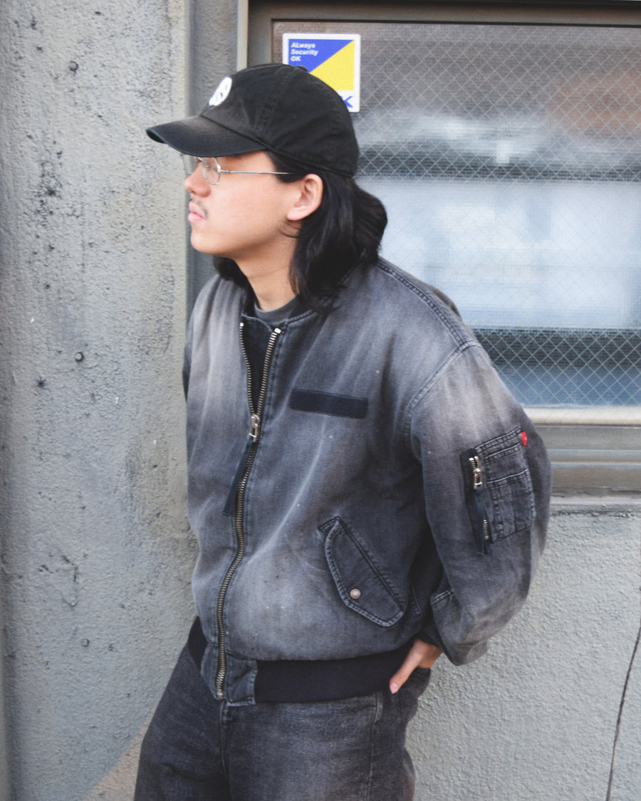 【 商品名：エイジングデュアルデニムMA-1 】

本製品は、ブランドのメイン素材であるデニムを使用し、ディティールを忠実に再現しながらシルエットを整えたブラックカラーのMA-1ジャケットです。中綿は入っていませんが、ライトオンスデニムを採用し、二重縫製によって柔らかく程よい肉感のある着心地に仕上げています。生地にはムラ糸を使用した8ozデニムを採用しており、シャープなムラ形状と粗野な風合いがより一層ヴィンテージ感を引き立てます。さらに加工には、全体にリアルなアタリ感を与えるエイジング加工を施し、深みのある表情を持たせています。