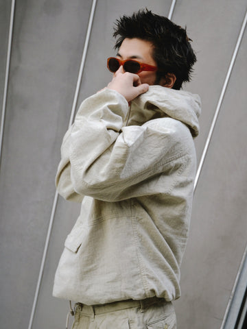 フード口のボタンの開閉により、首周りのニュアンスを自在に調整できる一着。素材には、麻カスや節を活かしたネップ糸を織り交ぜたコットンリネンチェックを採用しました。ドライタッチな生地にワンウォッシュを施すことで、麻特有のハリ感を残しつつ、肌馴染みの良い柔らかな風合いと豊かな表情を引き出しています。

This piece features adjustable hood buttons to alternate between a clean look and a relaxed neckline. Crafted from a cotton-linen check weave with rustic nep yarns, it highlights the natural texture of the fibers. The BEIGE fabric is one-washed to balance a crisp, dry touch with a soft, broken-in feel, creating a sophisticated yet comfortable aesthetic.