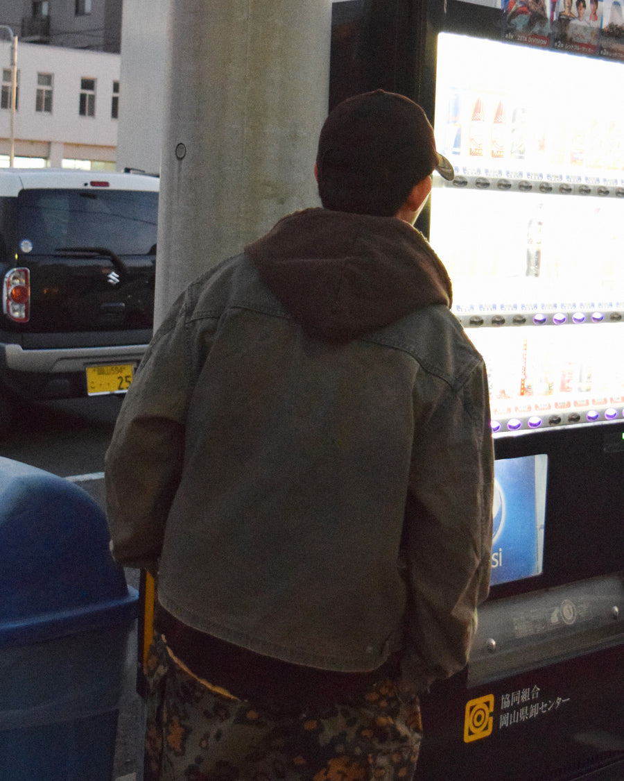 【 商品名：リメイクデトロイトダックジャケット 】

本製品は、ゆとりのある身幅とややクロップド丈に設計されたブラックカラーのジャケットで、インナーアイテムとのレイヤードを楽しめるバランスの良いシルエットが特徴です。生地には頒布の中でも最も薄手の11号帆布生地を採用しており、強度・耐久性に優れ、着用を重ねるごとにアタリなどの経年変化を味わえる素材です。さらに、水や薬品の使用量を抑えながら生地の凹凸部分のアタリを強調し、同時に自然な脱色感を生み出す特殊エイジング加工を施し、加えてサンフェードによるダメージ加工を加えることで、より奥行きのある表情に仕上げています。