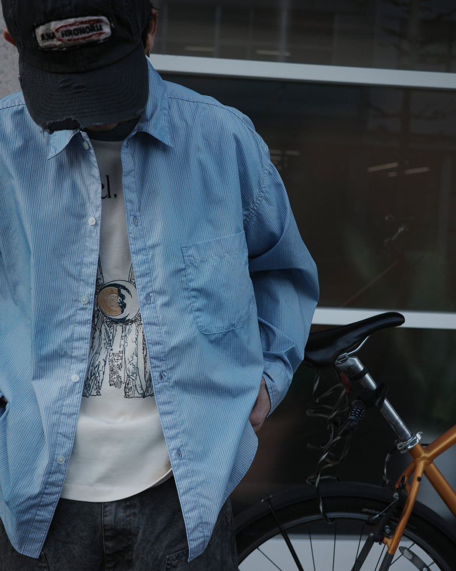 クリーンな高密度ストライプシャツに、スプレーによる顔料吹き付け加工を施し、自然なムラ感を与えた一着。リラックス感のあるシルエットが、上品さとラフさを絶妙なバランスで両立させています。素材には米綿100%の高密度ストライプ生地を採用。綿100%のナチュラルな風合いながら、シワになりにくい実用性も兼ね備えています。

A clean stripe shirt enhanced with a subtle pigment spray process for a natural, textured look. The relaxed silhouette perfectly balances elegance with a casual edge. Crafted from high-density US cotton stripe fabric, this BLUE STRIPE piece offers a crisp feel that is naturally wrinkle-resistant while maintaining the comfort of 100% cotton.