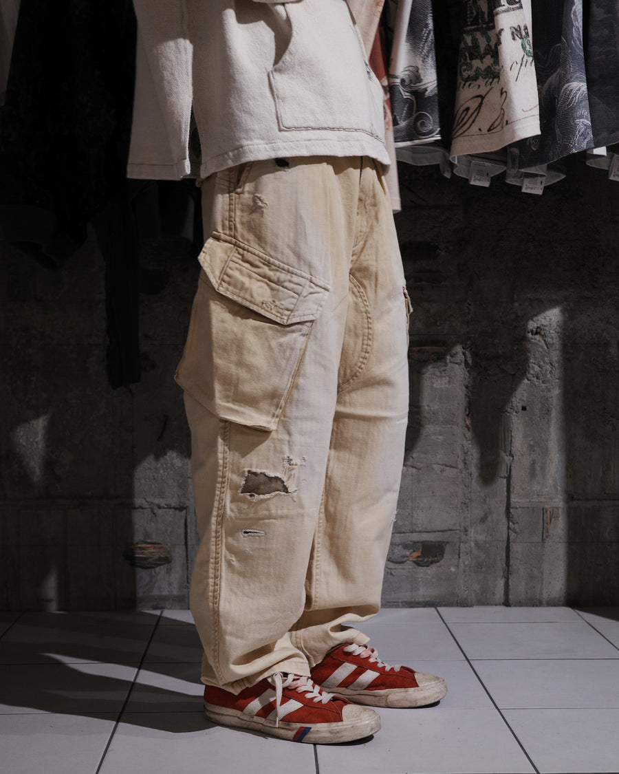 ミリタリートラウザーズを現代的にリファイン。斜めのカーゴポケットが実用的なアクセントを添え、洗練されたテーパードラインが際立ちます。素材には肌馴染みの良い10sヘリンボンを採用。環境に配慮した特殊エイジング・サンフェード加工と随所のリメイクにより、リアリティのある褪色感とヴィンテージな佇まいを表現しました。

Modernized military trousers with a refined tapered fit and slanted cargo pockets. Crafted from soft 10s herringbone, this KHAKI pair features special sun-fading and remake details. It achieves an authentic, time-worn vintage character while utilizing eco-conscious processing to minimize environmental impact.