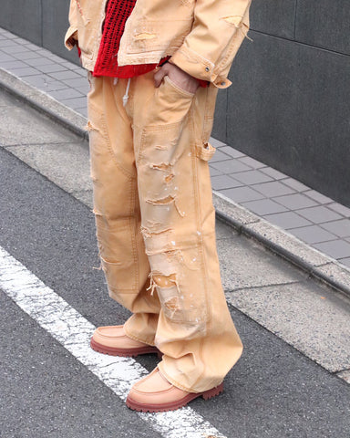 【 商品名：リメイクダブルニーダックペインターパンツ 】

本製品は、レングスをやや長めに設定したイエローカラーのペインターパンツです。ウエスト部分にはナイロンオックス生地で切り替えを施し、ワーク感を抑えたバランスの良いデザインに仕上げています。生地には頒布の中でも最も薄手の11号帆布生地を使用しており、強度・耐久性に優れるだけでなく、着用を重ねるごとにアタリなどの経年変化を味わえる素材です。また、水や薬品の使用量を抑えながら生地の凹凸部分のアタリを強調し、同時に自然な脱色感を与える特殊エイジング加工に加え、サンフェードによるダメージ加工も施すことで、より深みのある表情に仕上げています。