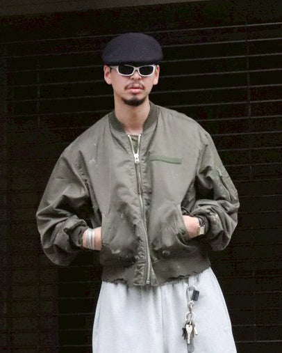 忠実なディテールを保ちながら、シルエットを現代的に整えたMA-1ジャケット。加工によりヴィンテージの風合いを再現した一着です。肉厚でミリタリーらしいツイル生地を使用し、打ち込みの密度や肌触りまでビンテージMA-1に近い仕上がりに。さらに、ダートペイントや特殊吹き付け、ダメージ加工を重ね、洗いをかけて染料を自然に剥がすことで、深みのある表情を生み出しています。カラーはオリーブ。