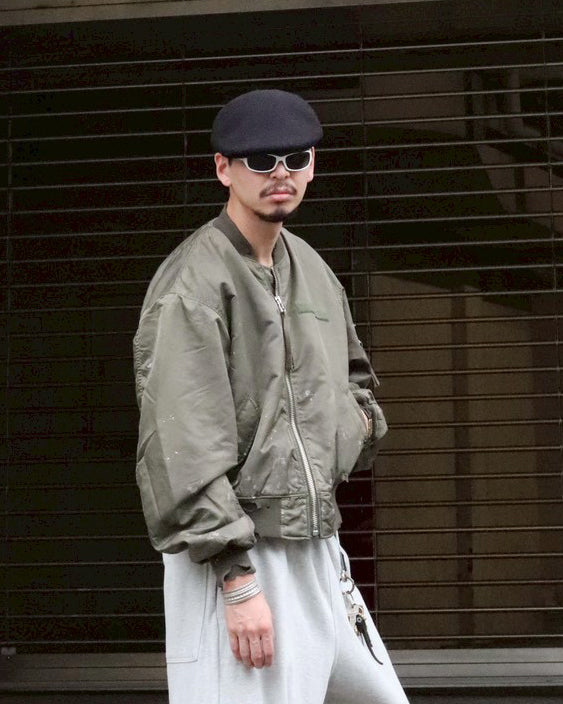 忠実なディテールを保ちながら、シルエットを現代的に整えたMA-1ジャケット。加工によりヴィンテージの風合いを再現した一着です。肉厚でミリタリーらしいツイル生地を使用し、打ち込みの密度や肌触りまでビンテージMA-1に近い仕上がりに。さらに、ダートペイントや特殊吹き付け、ダメージ加工を重ね、洗いをかけて染料を自然に剥がすことで、深みのある表情を生み出しています。カラーはオリーブ。