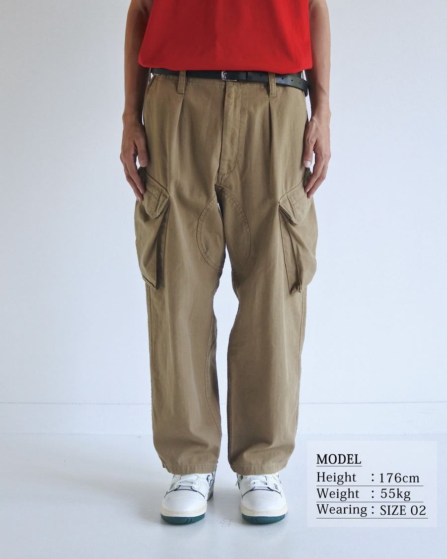 ミリタリートラウザーズをベースに、シルエットを現代的にリファイン。印象的な斜めのカーゴポケットが、立体感と実用性を両立させています。裾にかけて緩やかに絞られたテーパードラインにより、無骨ながらも洗練された印象に。素材には肌馴染みの良い10sヘリンボンを採用し、ストーンバイオウォッシュで柔らかな風合いとこなれ感を引き出しました。

Military trousers refined with a modern tapered silhouette. The distinctive slanted cargo pockets offer both practical utility and a structured look. Crafted from soft, classic 10s herringbone, this KHAKI pair has been treated with a stone bio-wash, providing a comfortable, worn-in texture and a sophisticated take on rugged style.